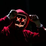 A spooky illuminated mask figure with a red hoodie in a dark setting, perfect for Halloween themes.